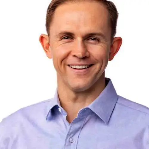 Smiling man in a light blue button-up shirt against a white background