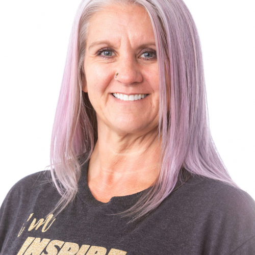 Smiling woman with long lavender hair wearing a dark graphic T-shirt on a white background