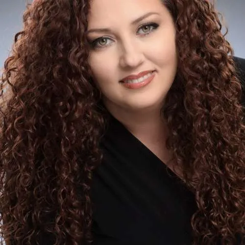 Portrait of a smiling woman with long curly hair wearing a black top against a gray background