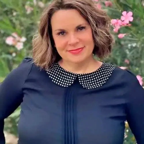 Woman in navy top with white polka-dot collar, smiling outdoors among pink flowers