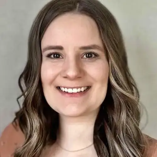 Smiling woman with wavy brown hair against a plain gray background