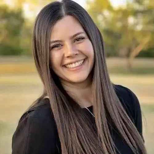 Smiling woman with long dark hair outdoors in a park at sunset