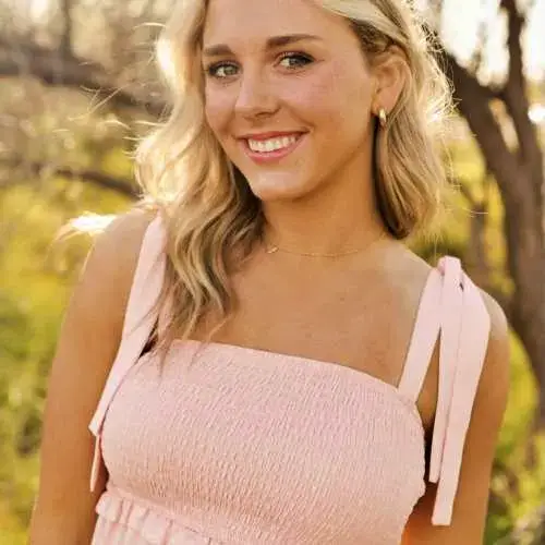 Smiling blonde woman in a pink dress standing outdoors in warm sunlight
