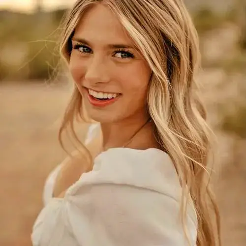 Smiling blonde woman in a white top outdoors with a soft, warm background