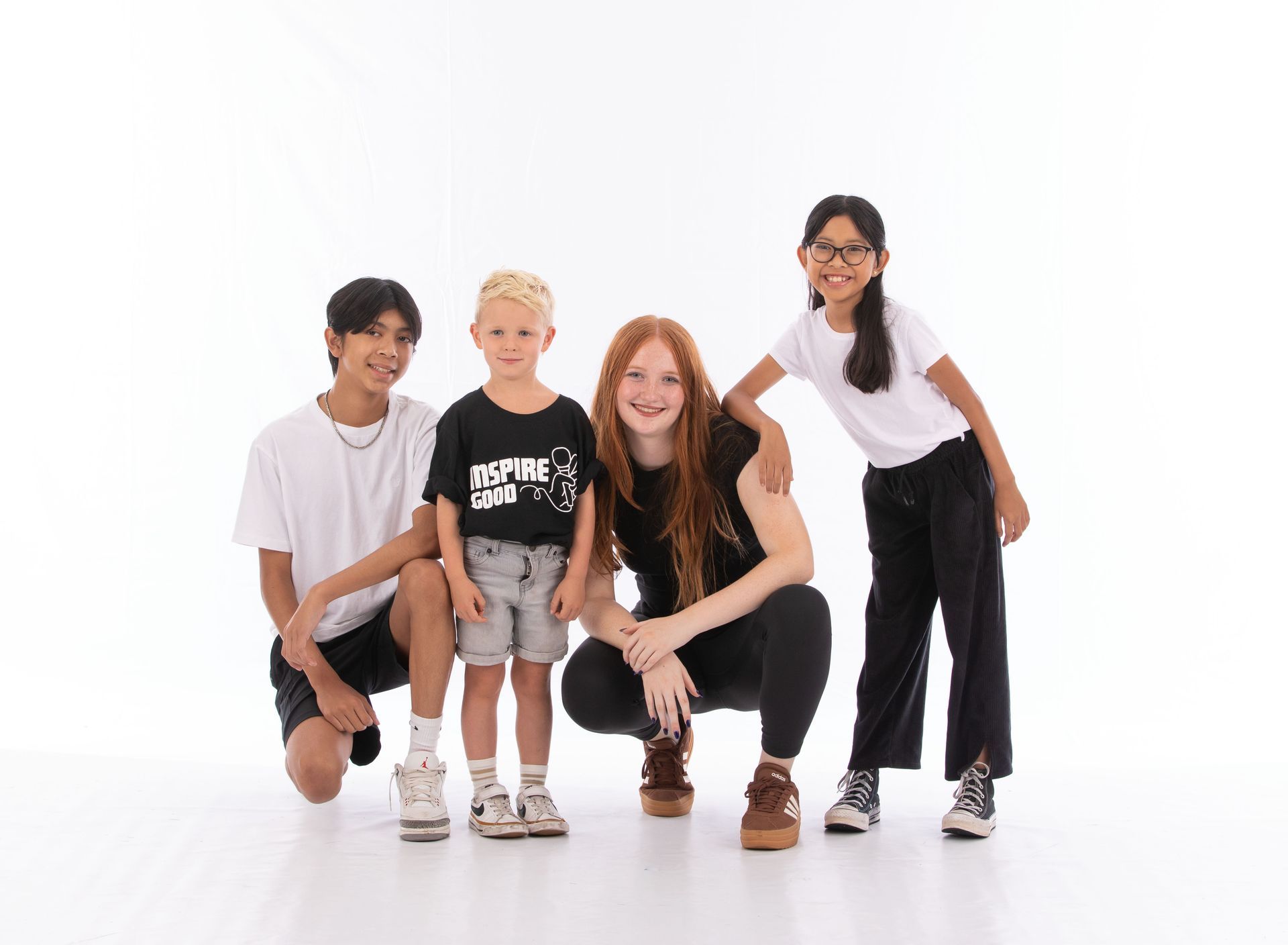 Four people crouch together in a bright studio, smiling at the camera.