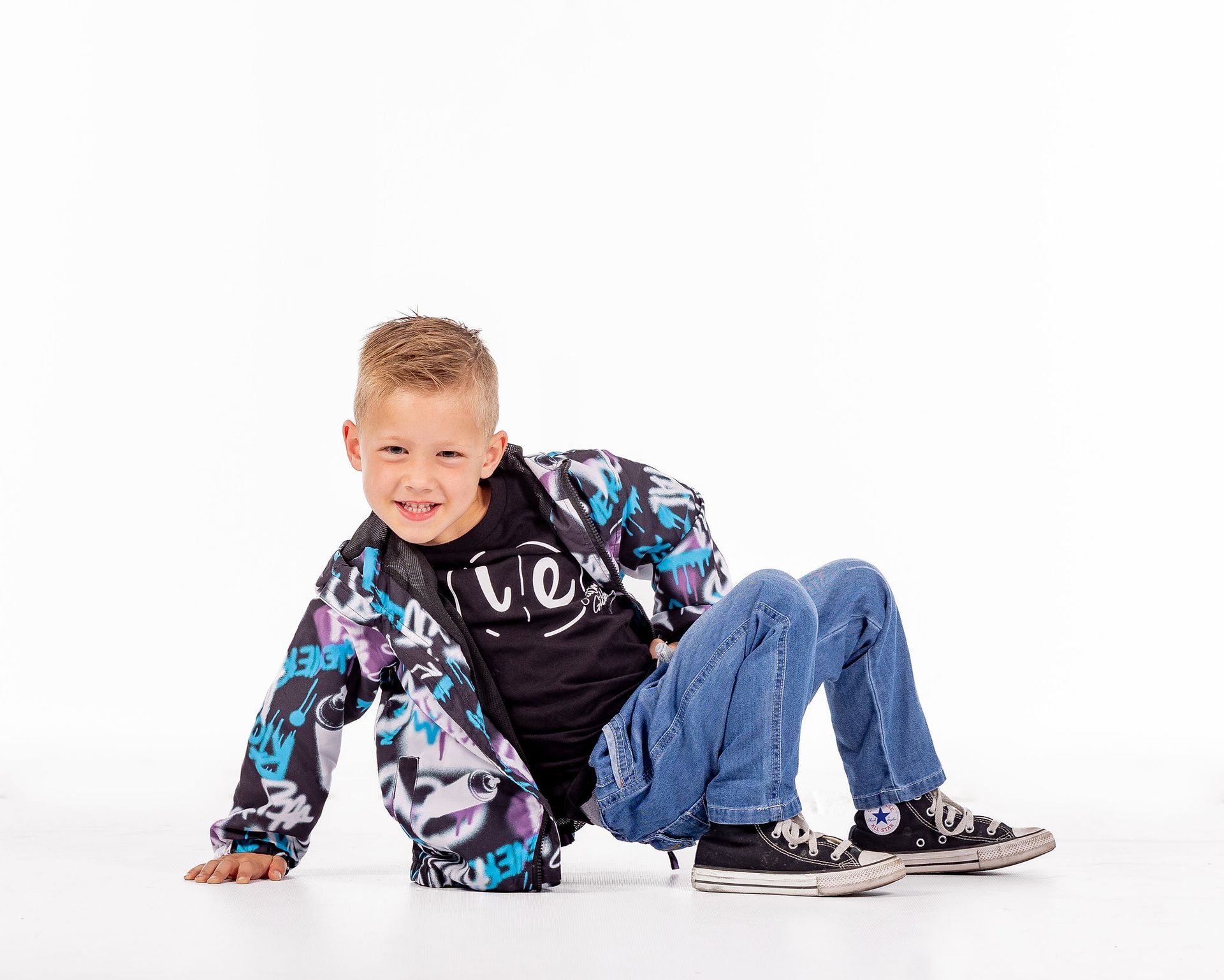 Smiling child in a colorful jacket and jeans reclining on a white studio background