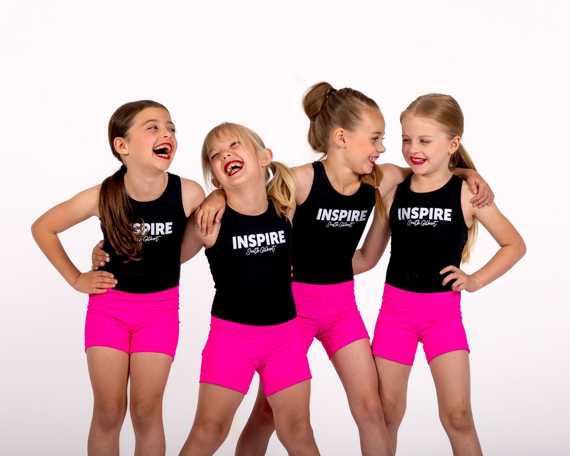 Four children in black tops and bright pink shorts pose together, smiling against a white background.