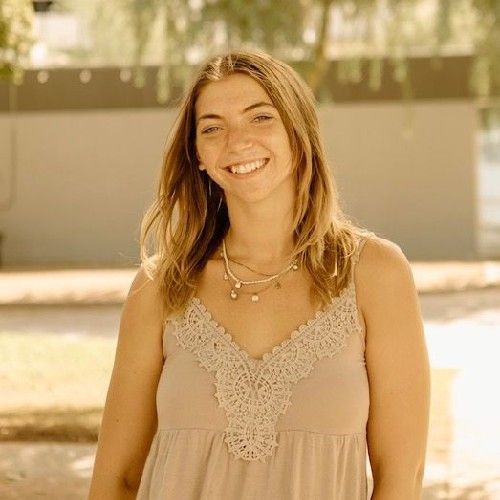 Smiling woman in a beige dress standing outdoors in warm sunlight