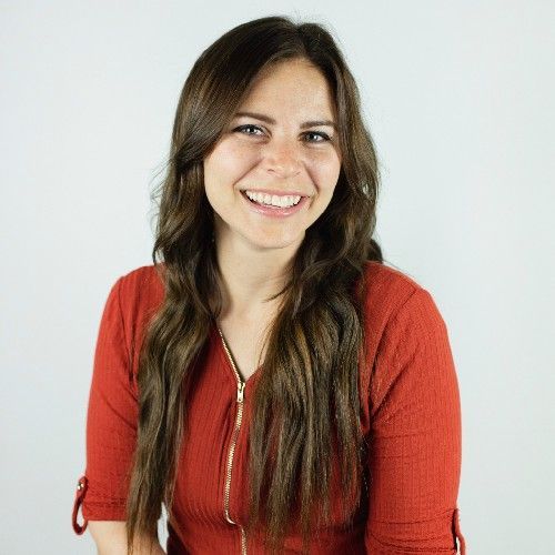 Smiling woman with long brown hair wearing a red top against a white background