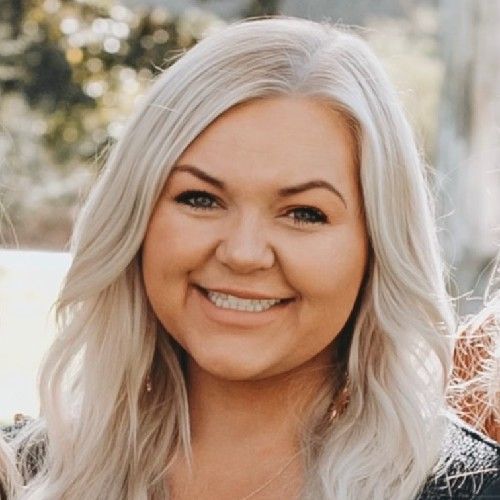 Smiling woman with long platinum blonde hair outdoors in soft sunlight