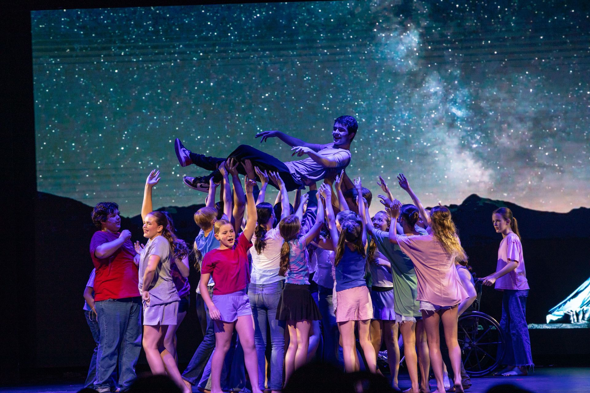 Group lifting a performer onstage under a starry night backdrop