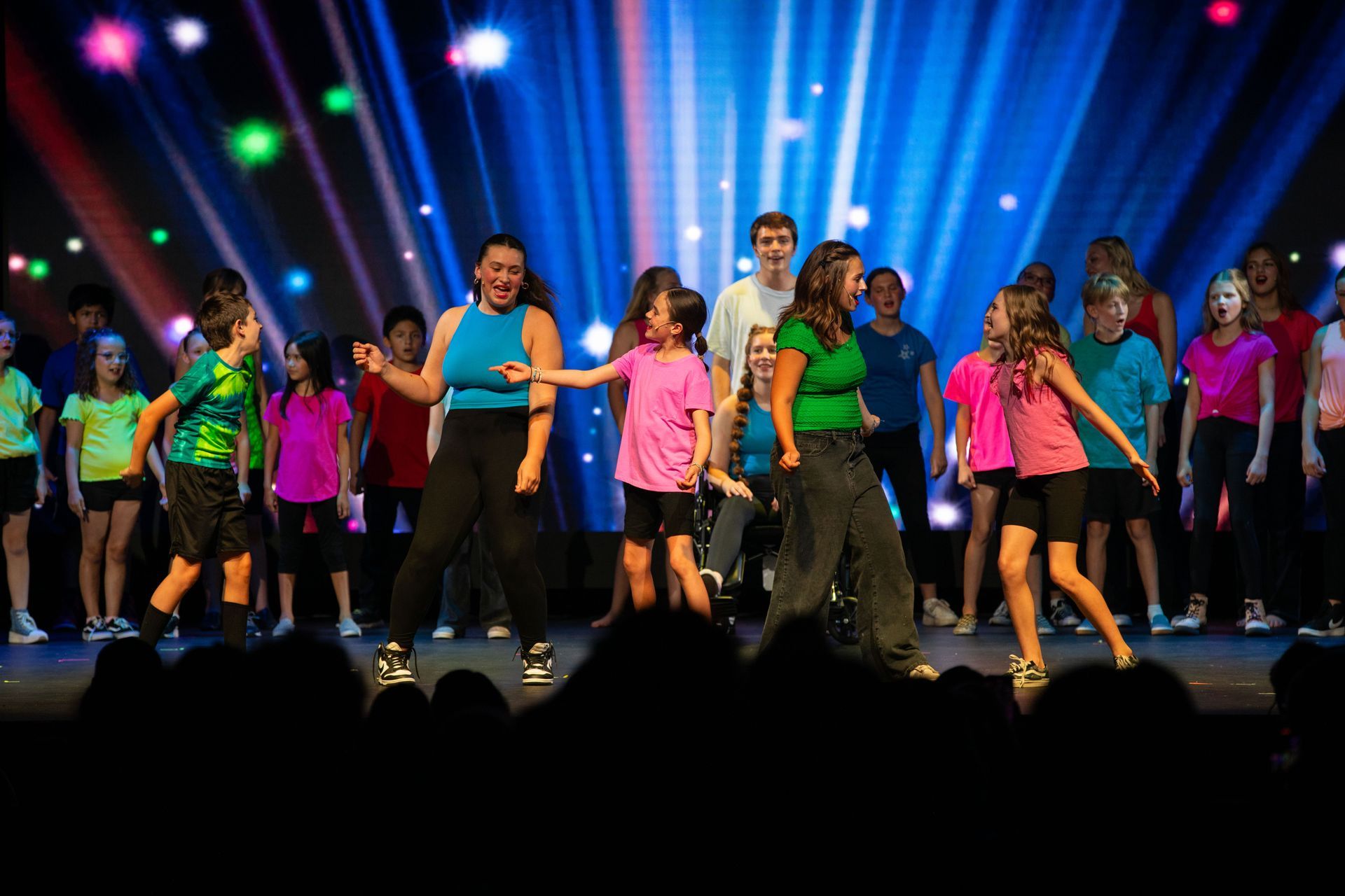 Dancers in colorful shirts performing onstage under blue and purple spotlights