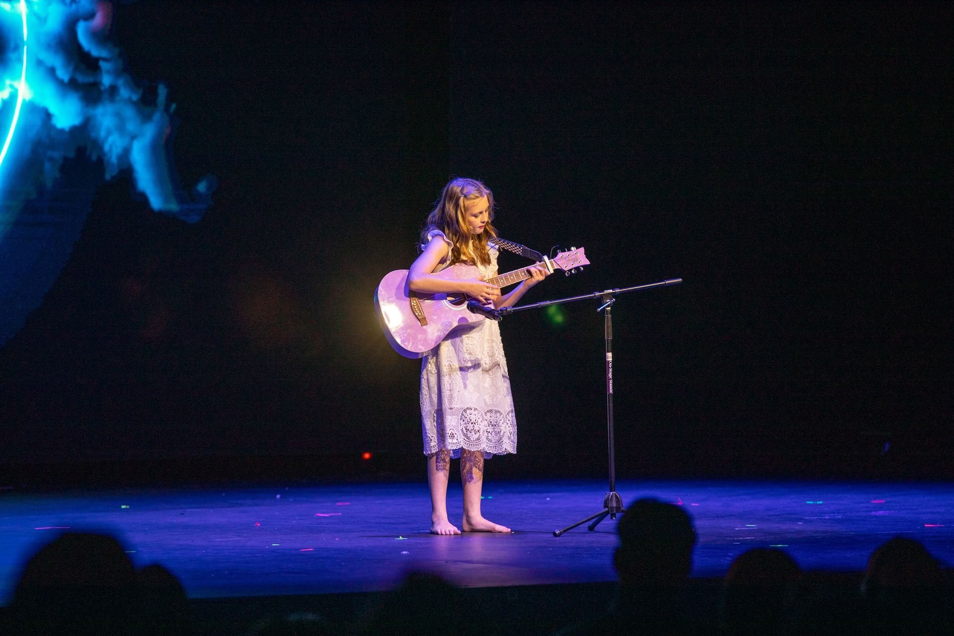 Musician playing guitar and singing on a dimly lit stage with blue lighting