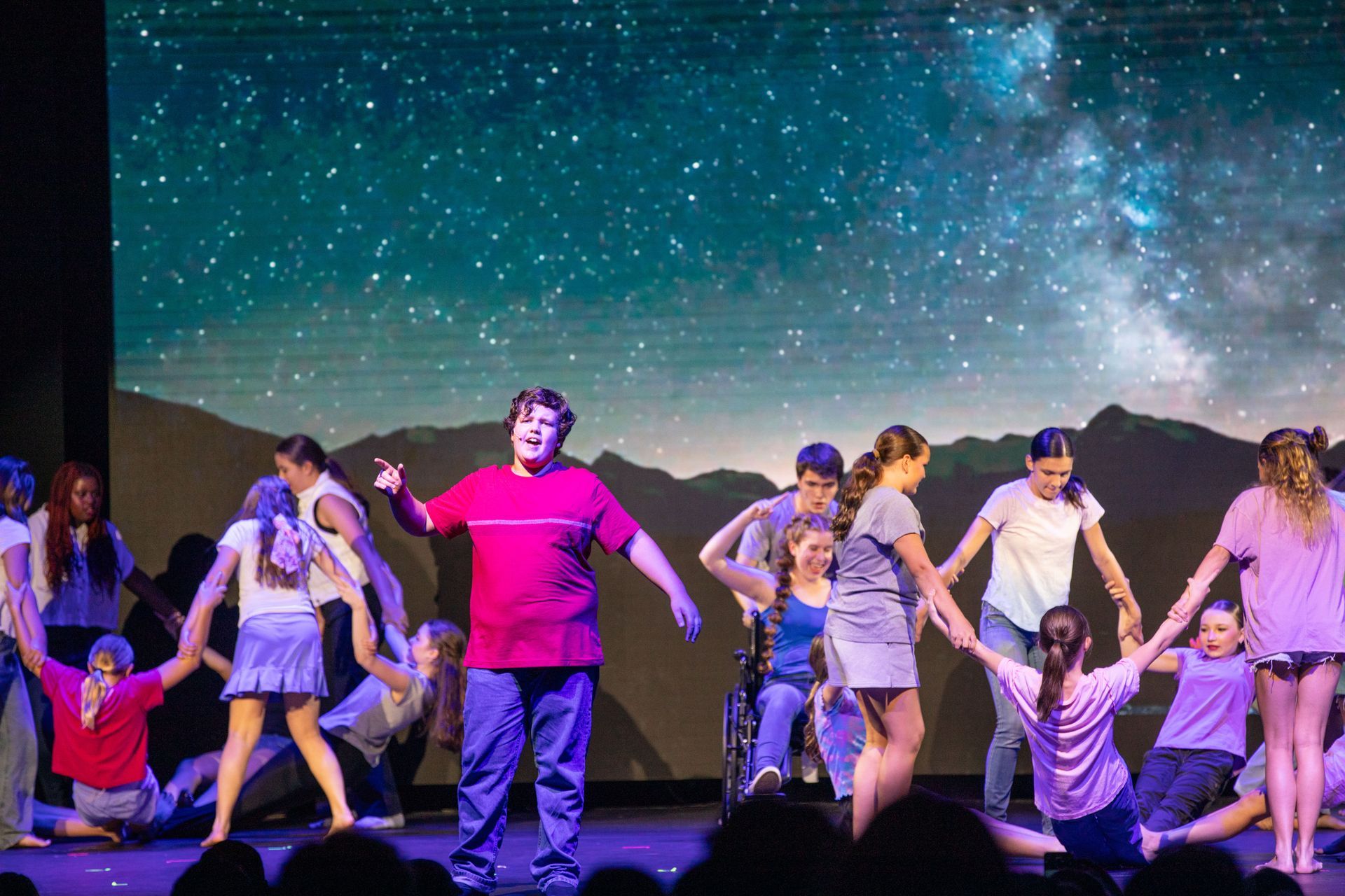 Stage dancers in colorful outfits performing under a starry night backdrop