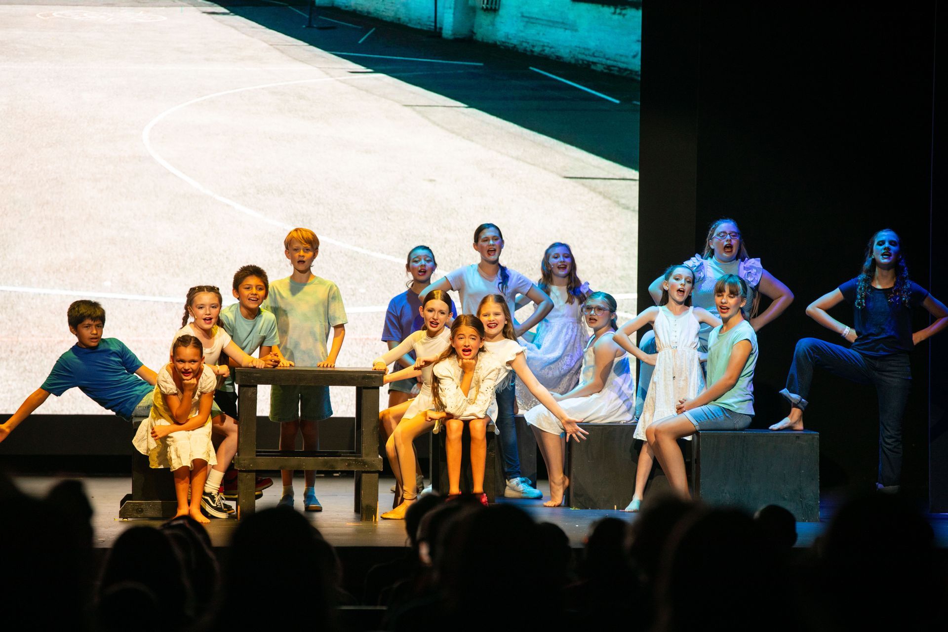 Group of children onstage performing a dance in colorful costumes under stage lights.