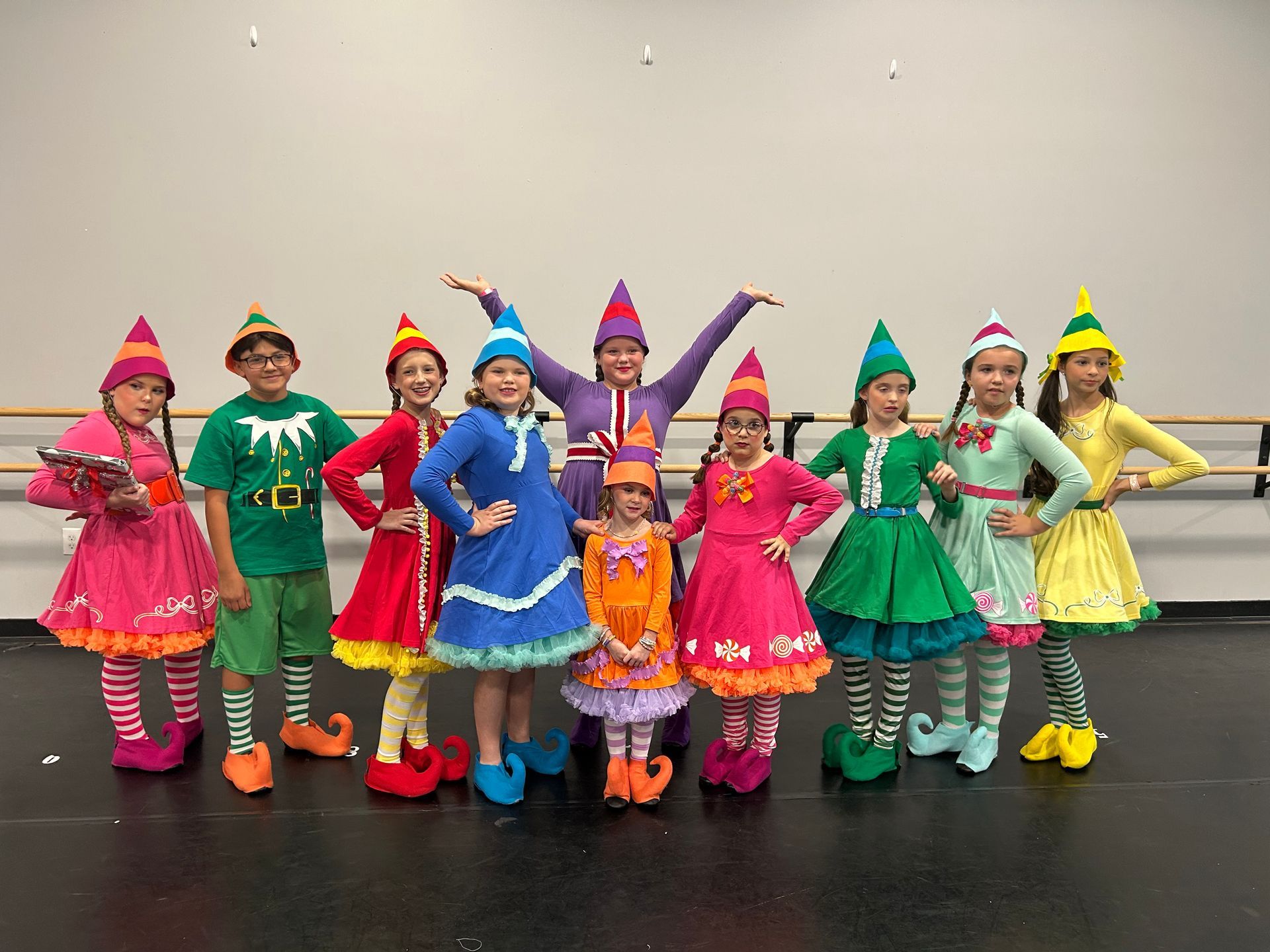 Group of children in colorful costumes and pointed hats posing indoors on a stage