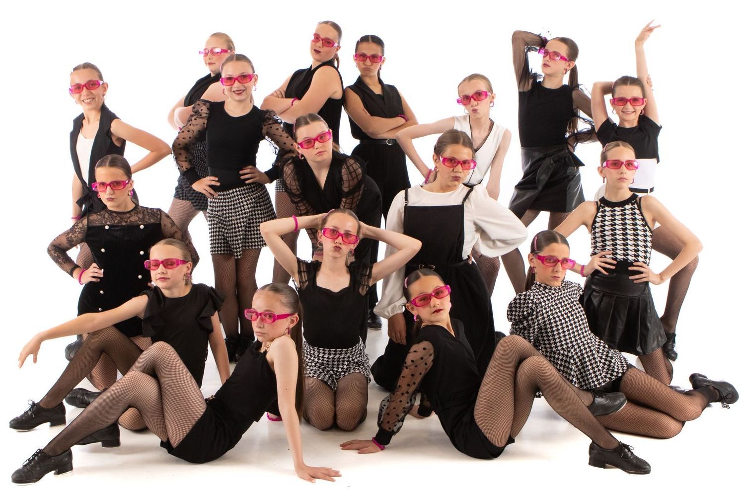 Group of dancers in black costumes and pink glasses posing in a studio against a white background