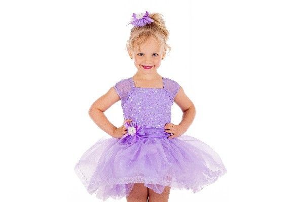 Child in a lavender tutu dress and flower hair accessory, standing with hands on hips against a white background