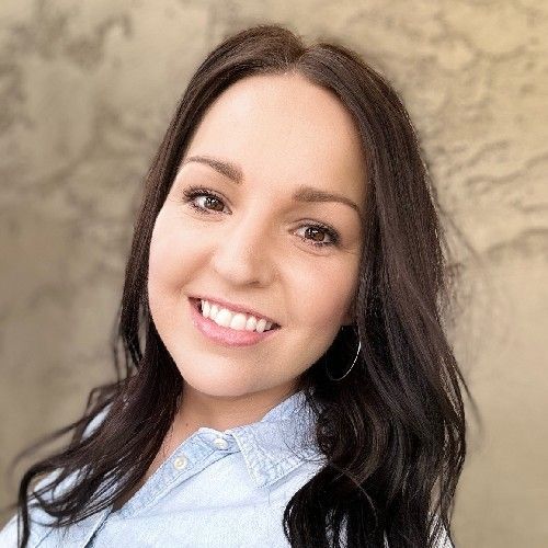 Smiling woman with dark hair in a light blue blouse against a beige textured background