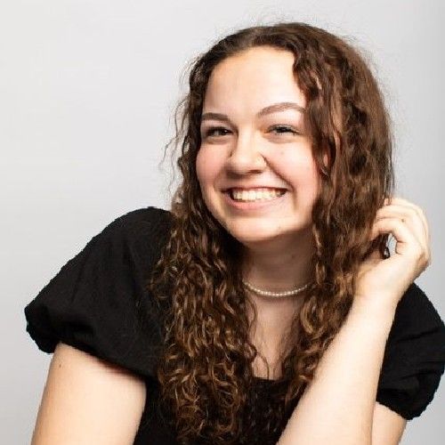 Smiling woman with curly hair in a black top against a light gray background