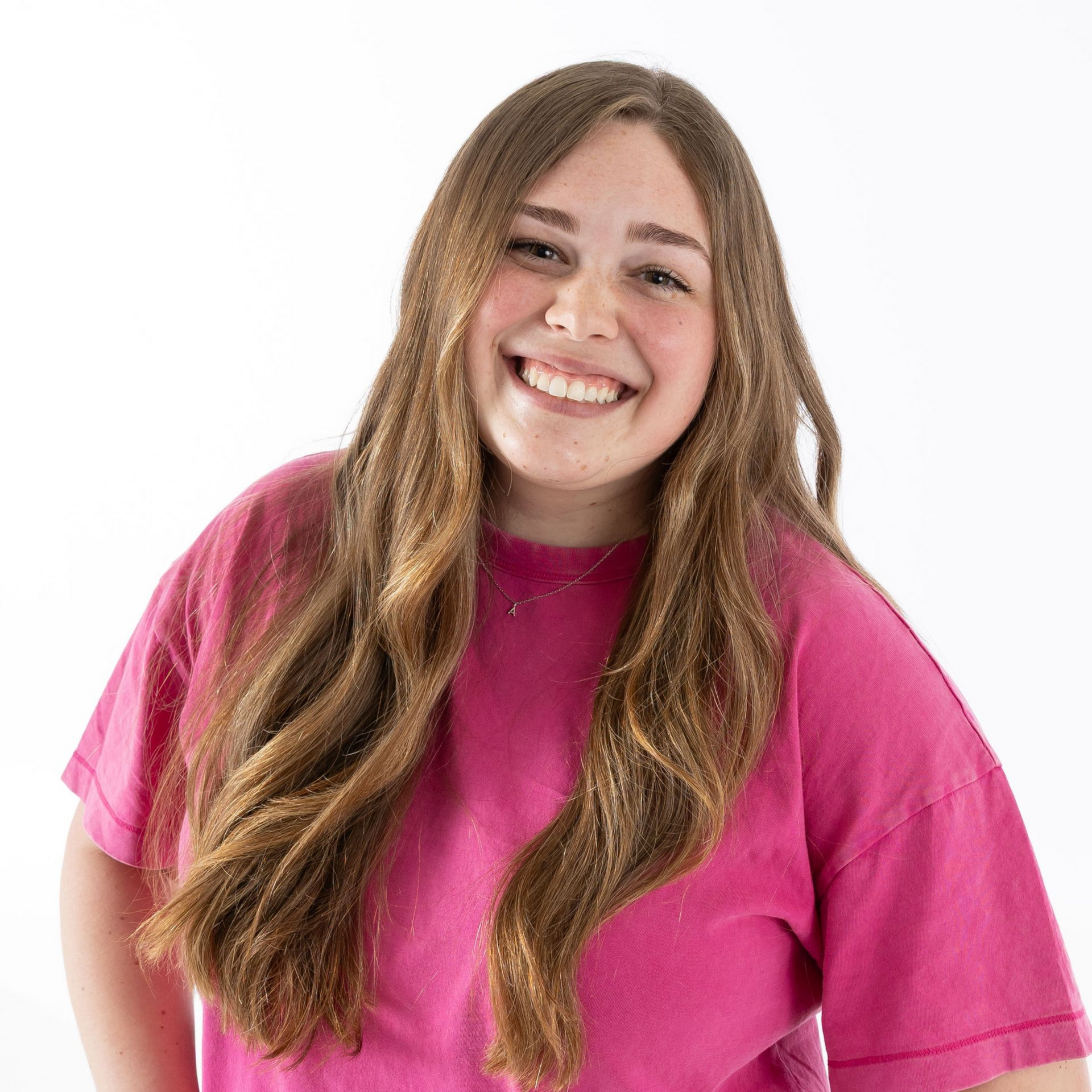 Smiling person with long hair wearing a bright pink shirt against a white background
