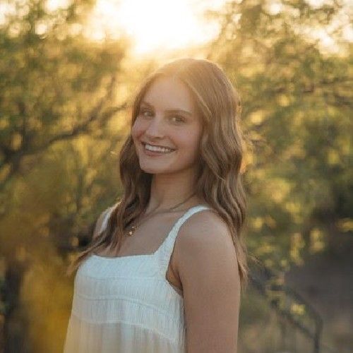 Smiling woman in a white dress standing outdoors at golden hour with blurred trees behind her