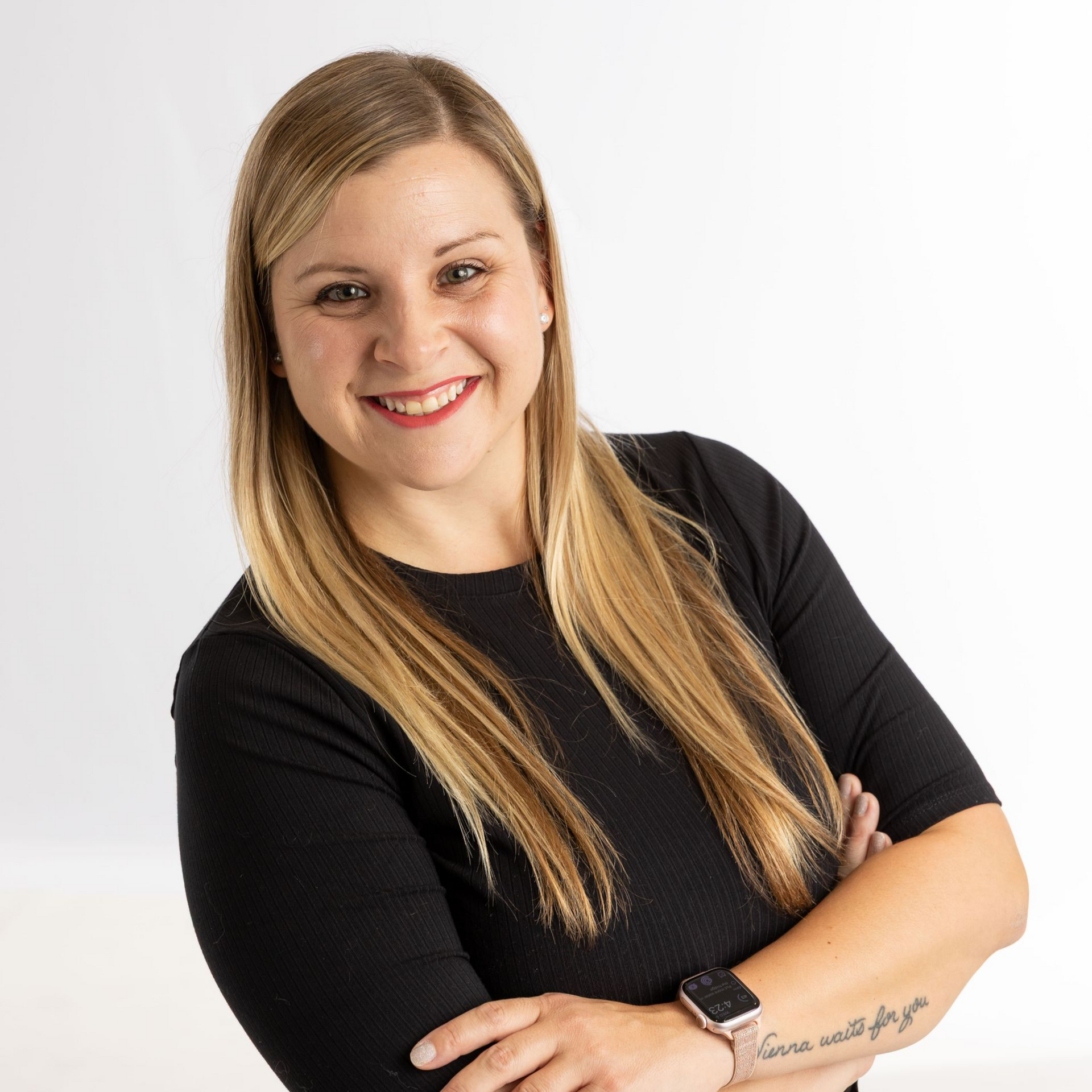 Smiling woman in a black top with arms crossed against a white background