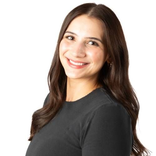 Smiling woman with long brown hair wearing a dark gray shirt against a white background