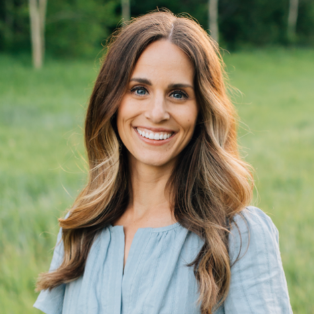 Smiling woman in a white dress standing outdoors at golden hour with blurred trees behind her