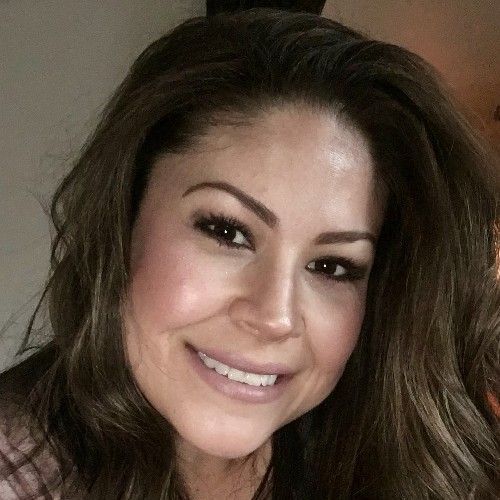 Smiling woman with long brown hair, wearing soft makeup against a neutral background