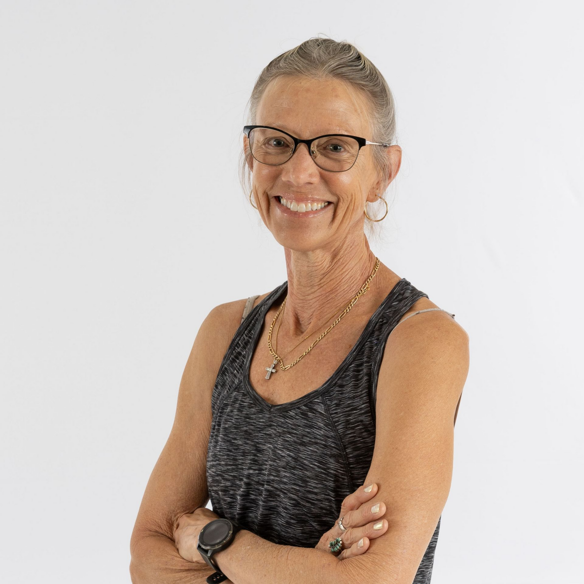 Smiling woman with glasses in a black sleeveless top, arms crossed against a white background