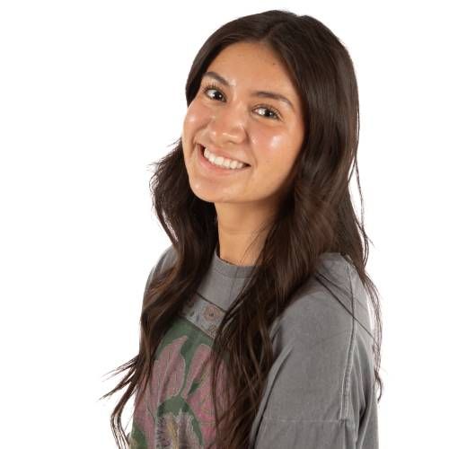Smiling person with long dark hair wearing a gray shirt against a white background