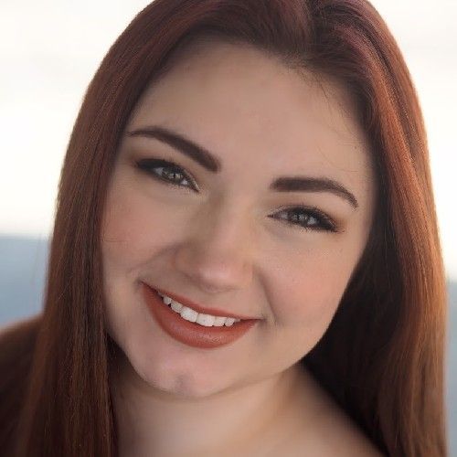 Close-up portrait of a smiling woman with auburn hair against a light background