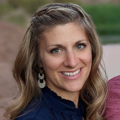 Smiling woman with wavy blonde hair wearing a navy top and dangling earrings outdoors