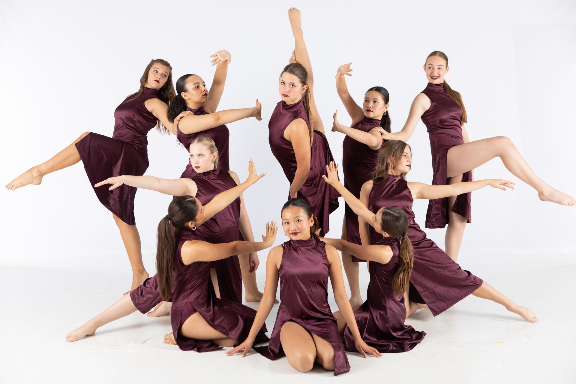 Dance team in matching burgundy costumes posing in a synchronized formation on a white background