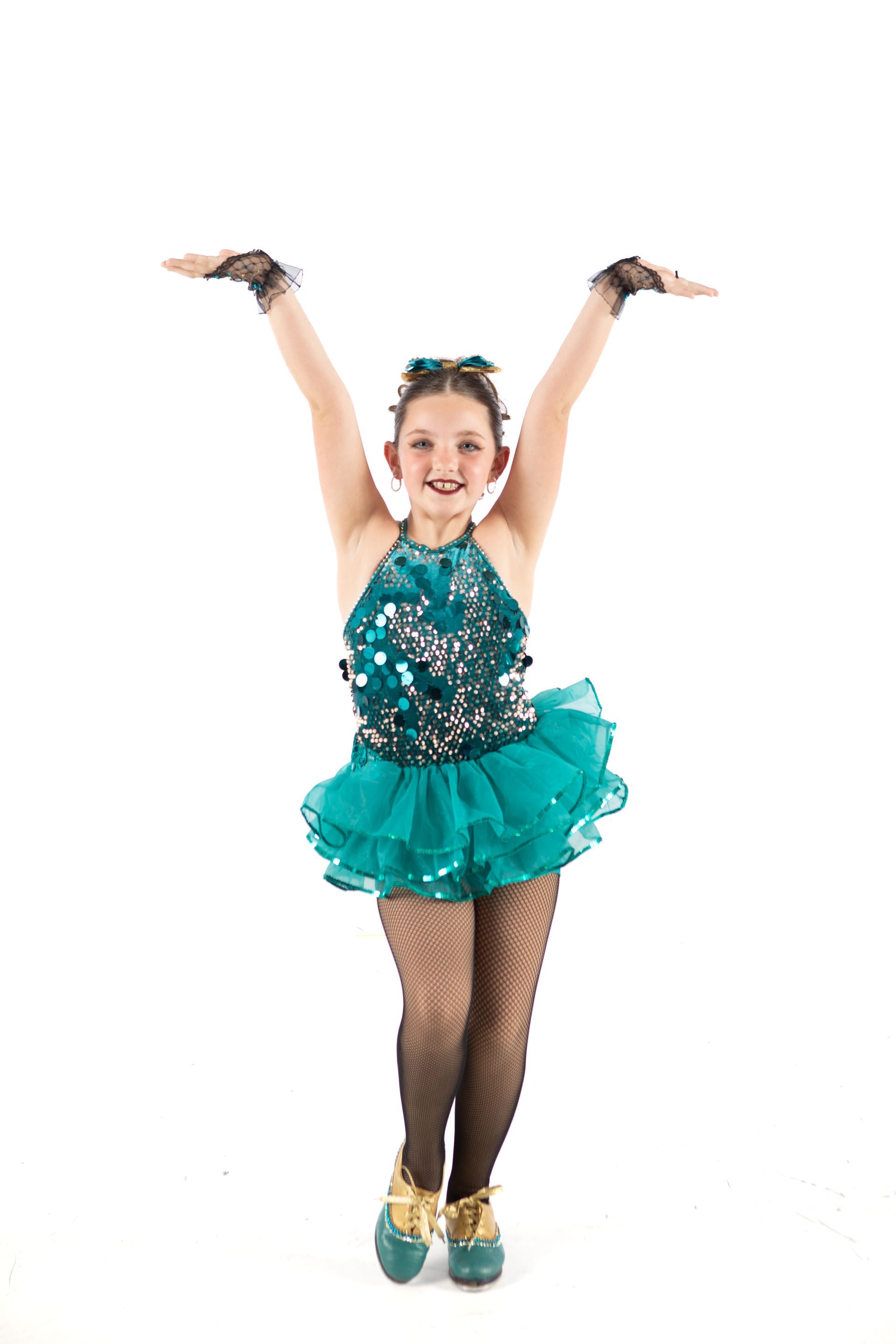 Young dancer in teal costume, arms raised, smiling on a white background.