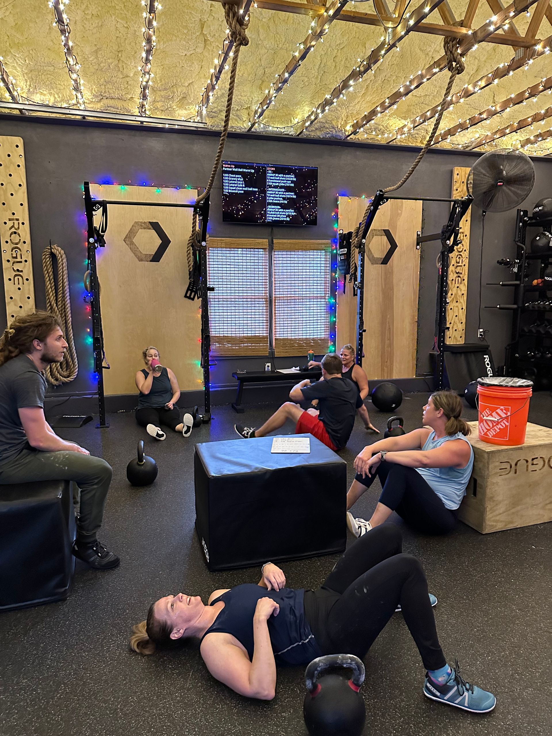 People exercising in a gym in Kennesaw, GA, lying on mats around a coach with a TV and kettlebell nearby