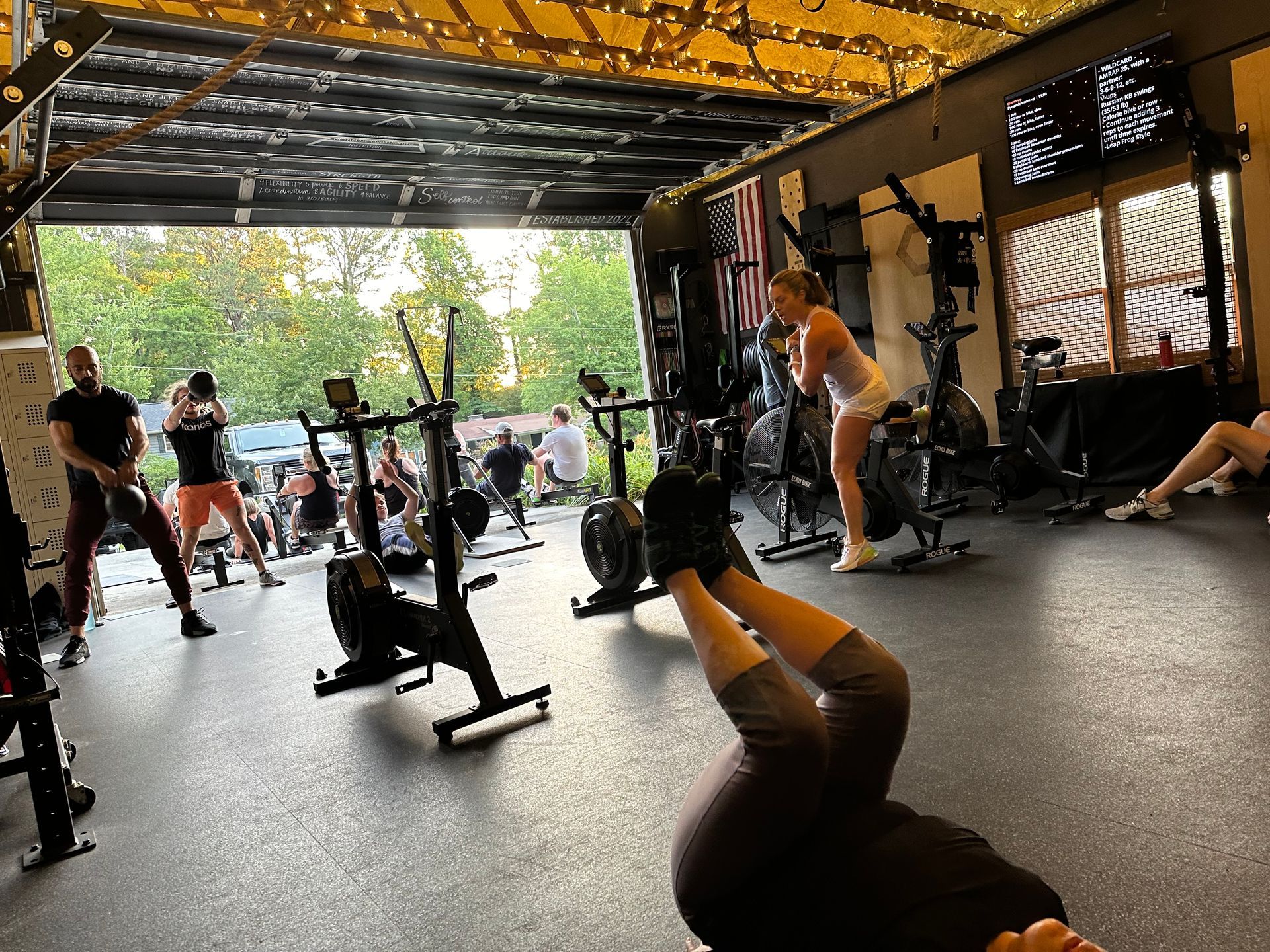 Indoor gym with people exercising on cardio machines and mats under a yellow-and-black covered roof in Kennesaw, GA.