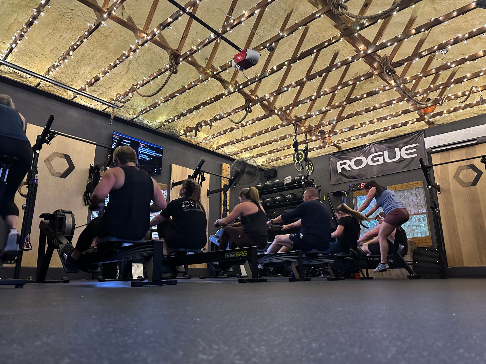 People exercising on rowing machines in a gym in Kennesaw, GA under a high wooden ceiling.