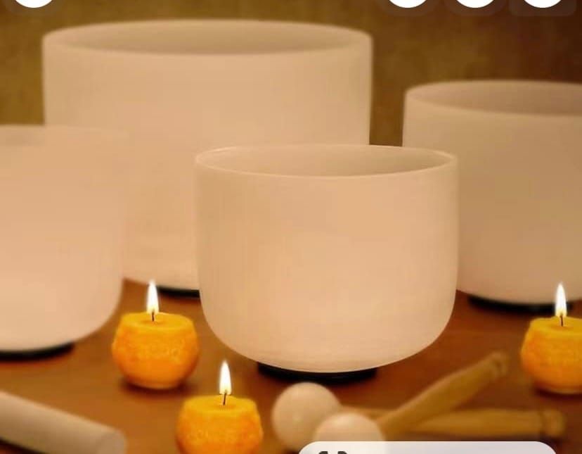 White singing bowls with lit tea candles on a wooden surface