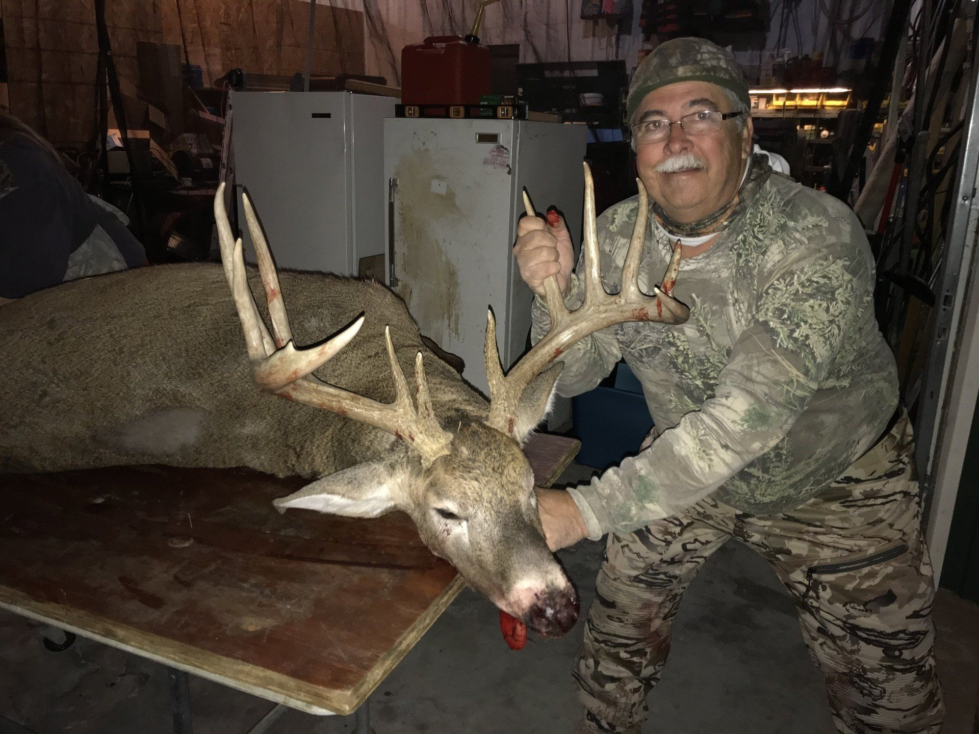 Man posing beside a large deer with antlers in a dim indoor setting