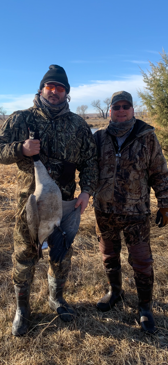 Two bundled-up people holding a duck outdoors in a snowy field under a blue sky