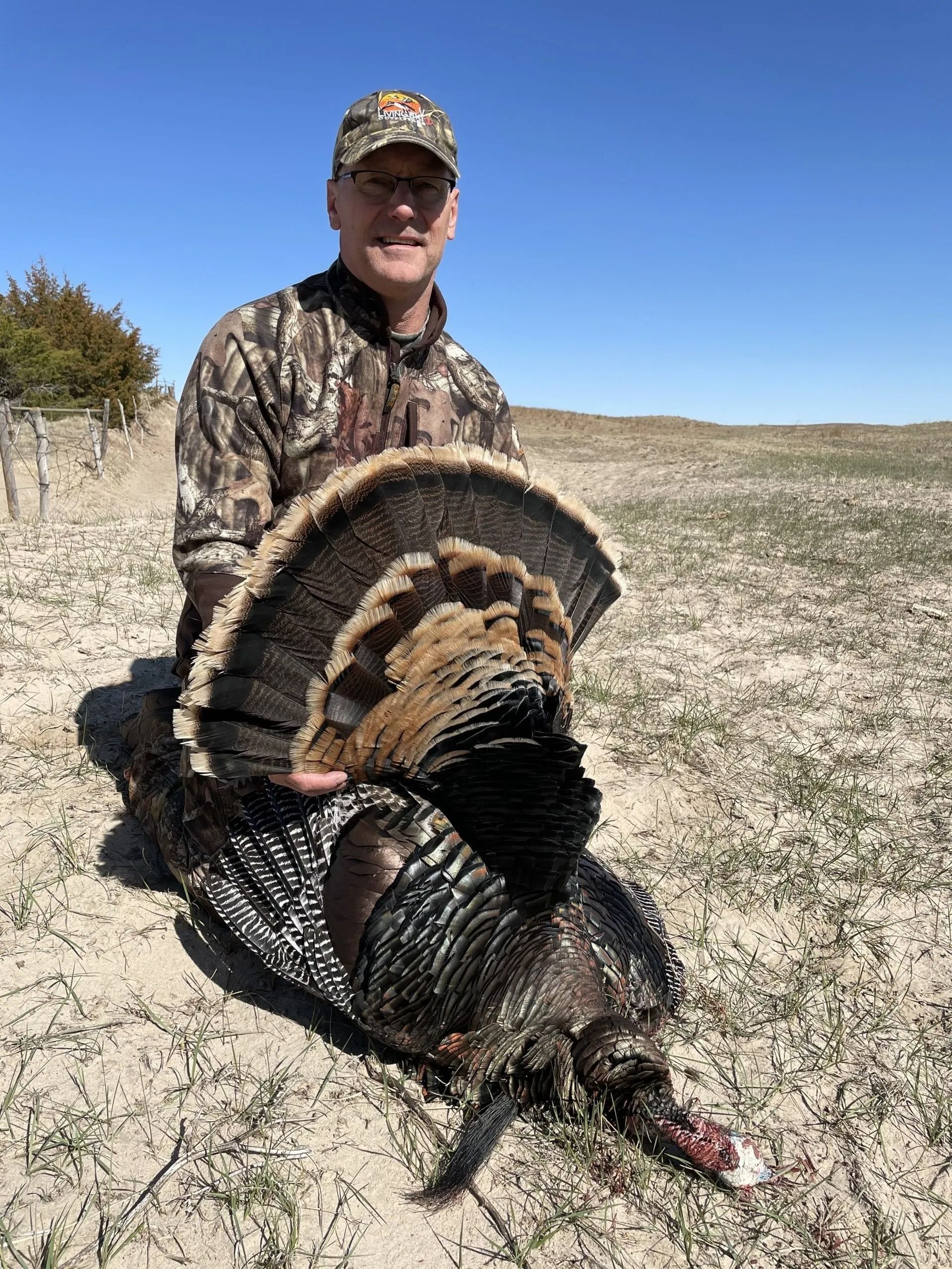 Hunter holding a large wild turkey in a grassy field under a clear blue sky