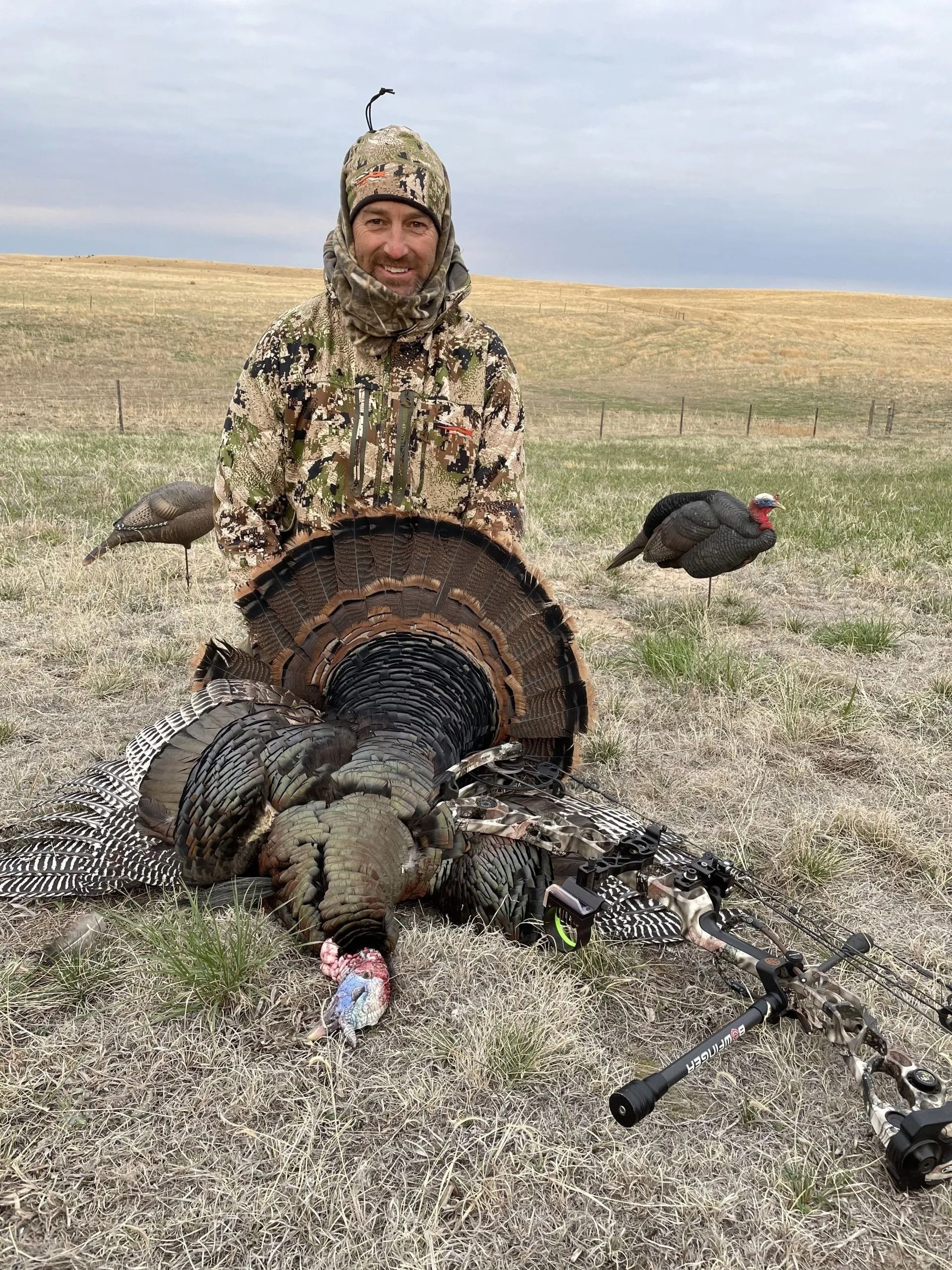 Hunter posing with a harvested turkey and hunting gear in a grassy field