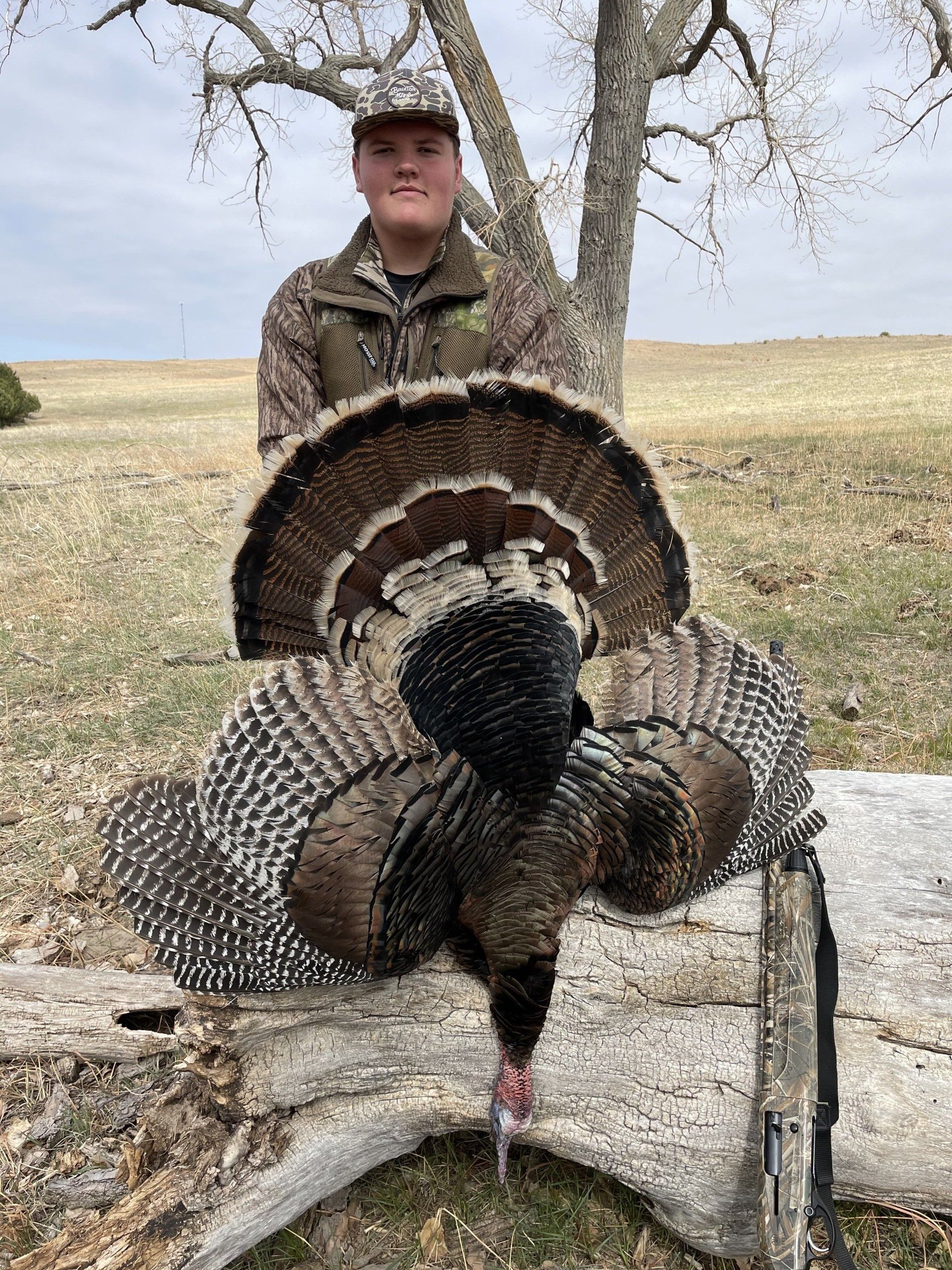 Hunter standing behind a large wild turkey with tail feathers fanned out in a field