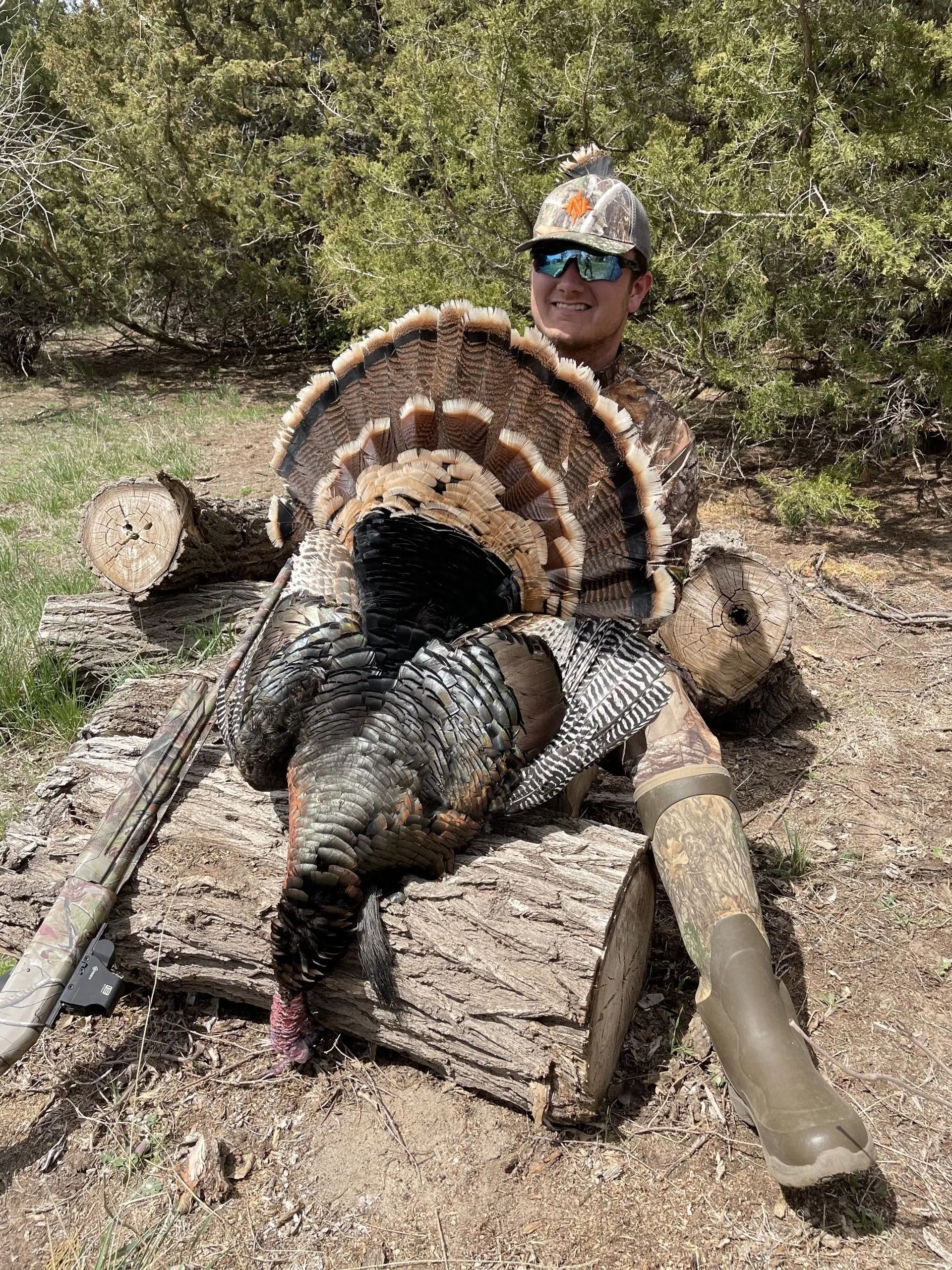 Hunter posing with a large turkey in a wooded outdoor setting