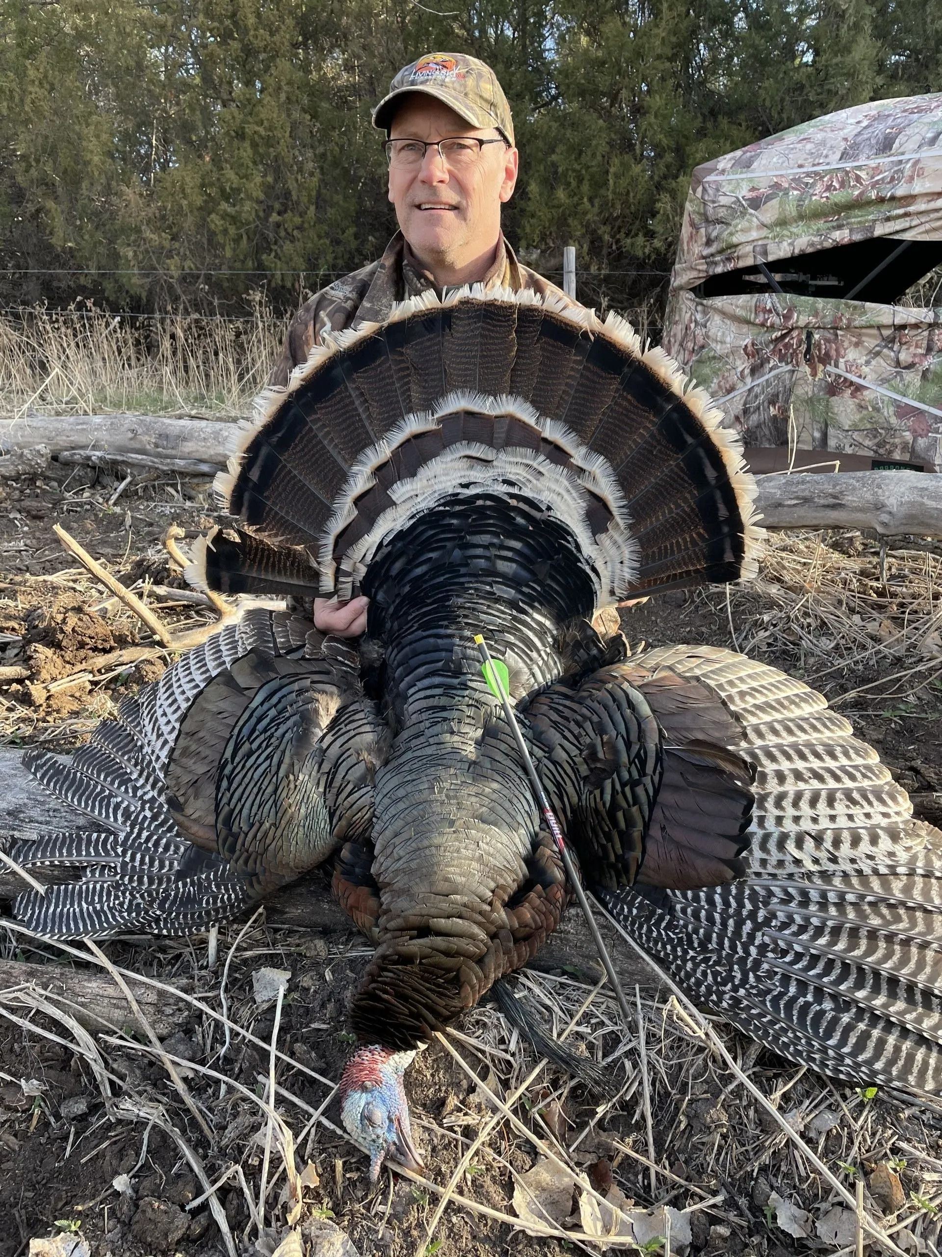 Man holding a large wild turkey by the tail in a dry, wooded field