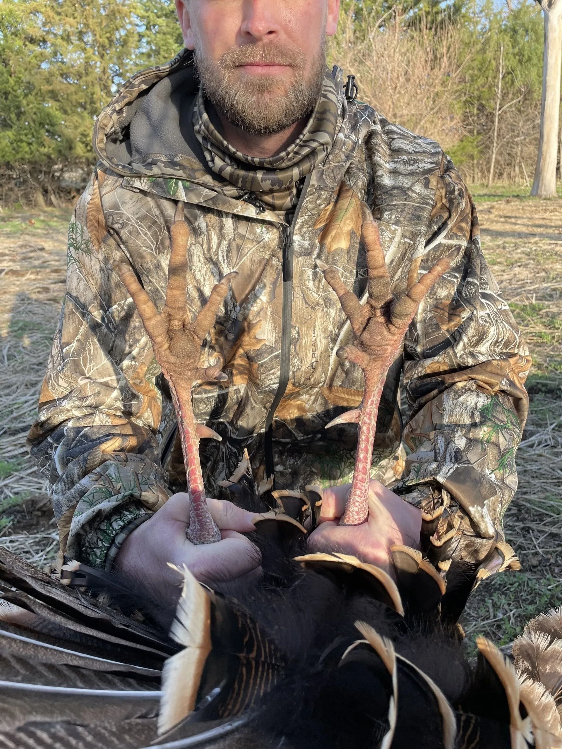 Person in camouflage jacket holding a deer by the antlers outdoors.