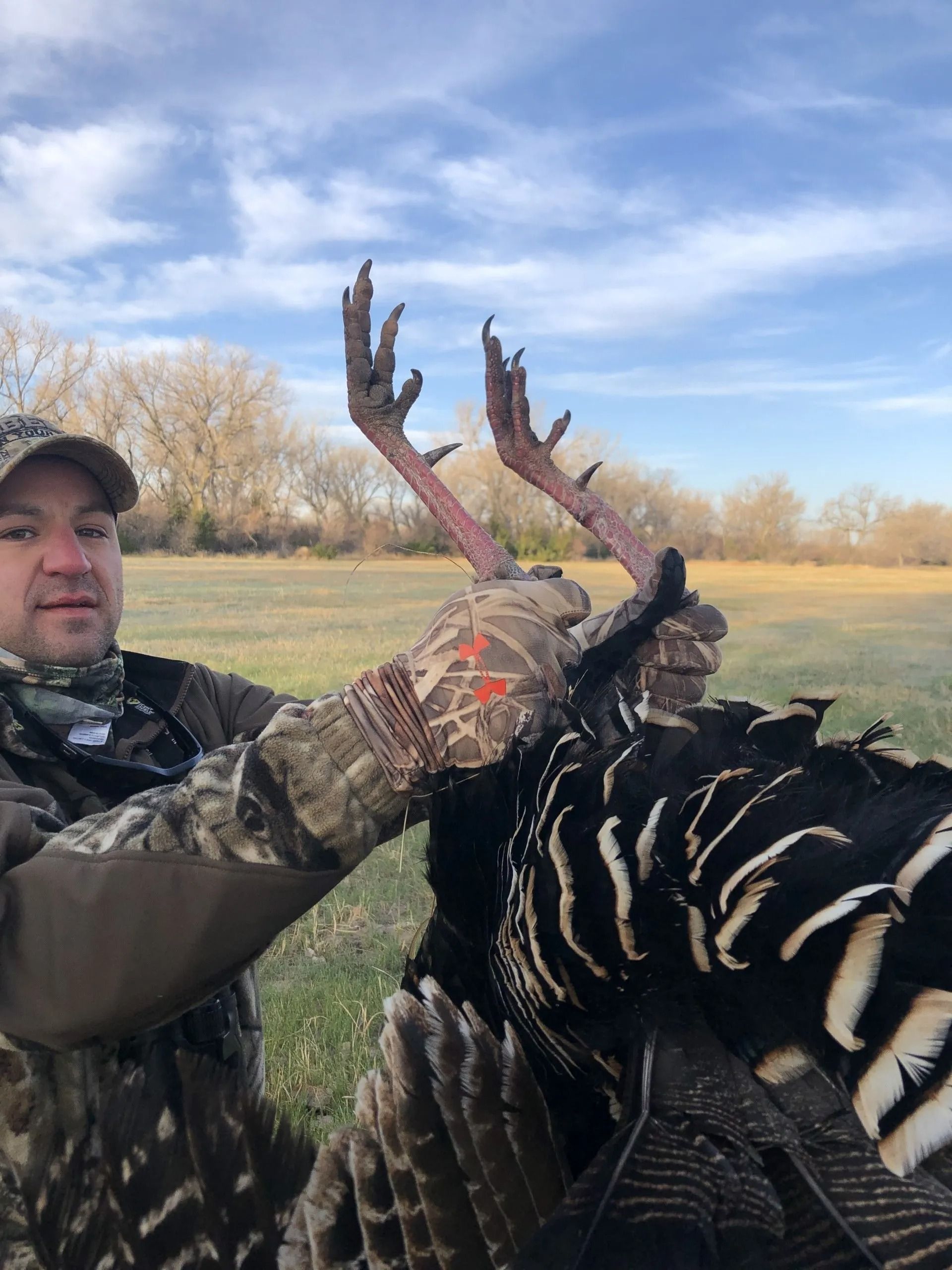 Hunter holding up a turkey in a grassy field under a blue sky