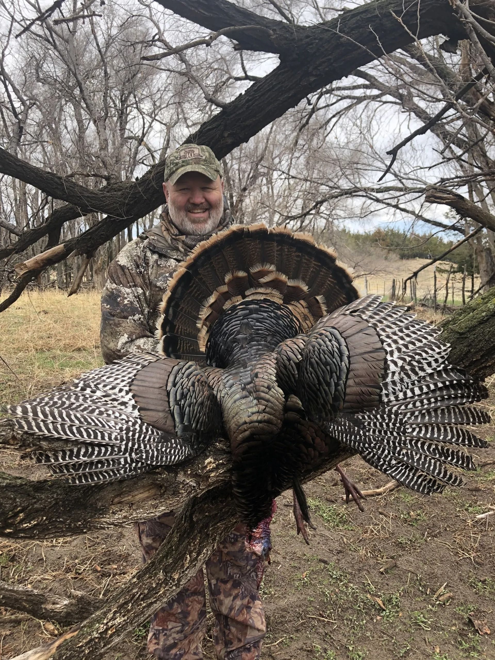 Hunter holding two large wild turkeys outdoors under bare tree branches